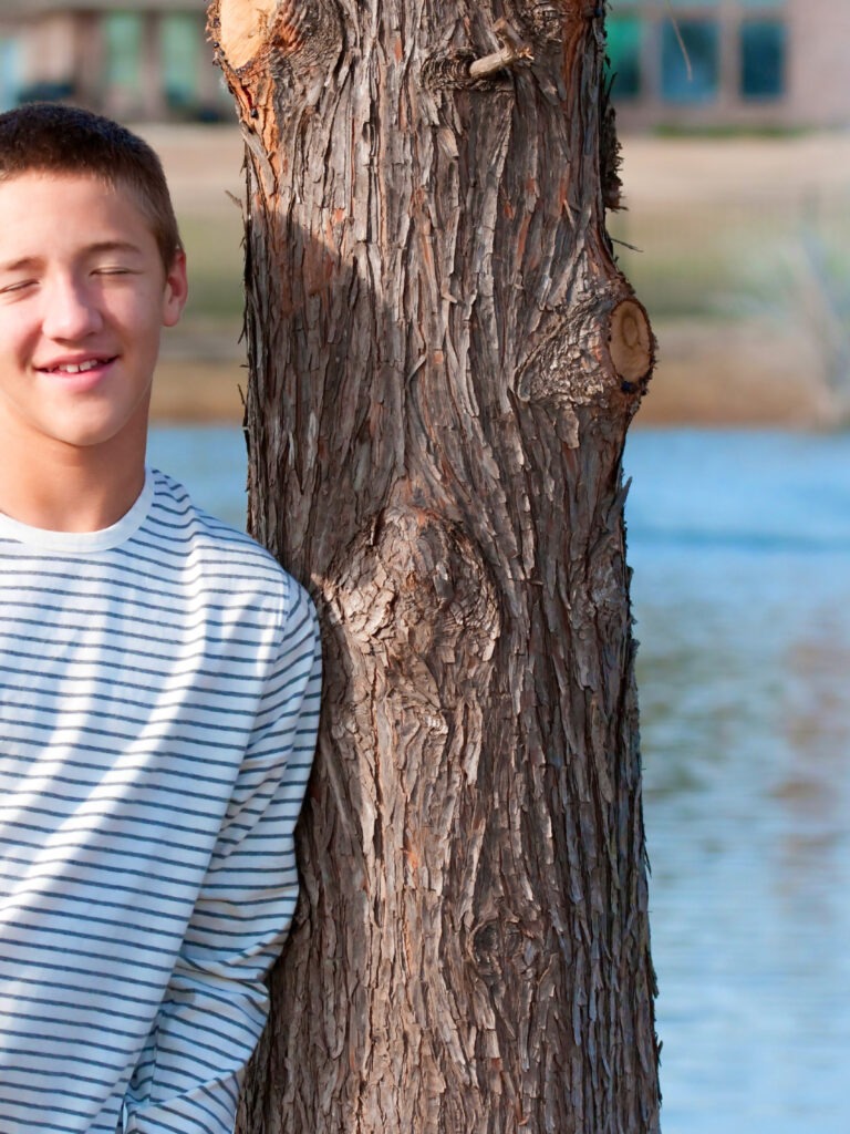Poika nojaa puuta vasten kesällä, taustalla järvi