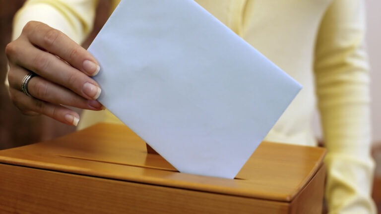 vaaliurna ja naisen käsi, joka laittaa siihen äänestyslipuketta