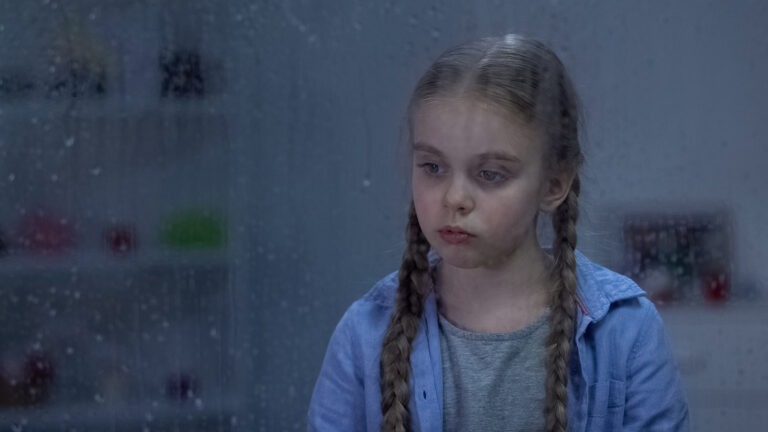 surullisen näköinen tyttö, jolla tukka leteillä, katsoo sateisen ikkunan läpi