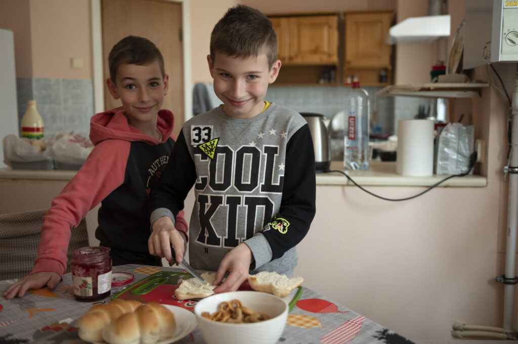 kaksi poikaa tekemässä voileipiä. lapset hymyilevät ja katsovat kameraan.