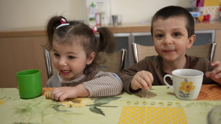 kaksi nuorta lasta ruokapöydän ääressä välipalalla
