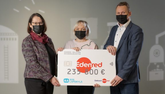 yksi tummatukkainen nainen , yksi vaaleatukkainen nainen ja tummahiuksinen mies puvussa pitävät isoa lahjasekkiä käsissään