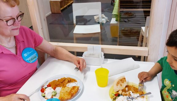 iäkkäämpi nainen pinkissa t-paidassa syö ruokaa pienen vihreäpaitaisen pojan kanssa