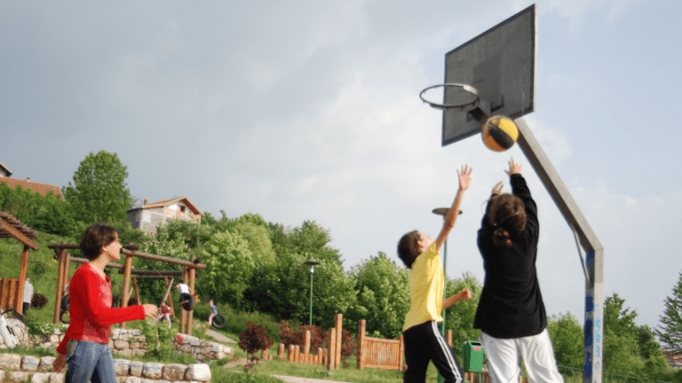 Lapsia ja nuoria pelaamassa koripalloa pihalla