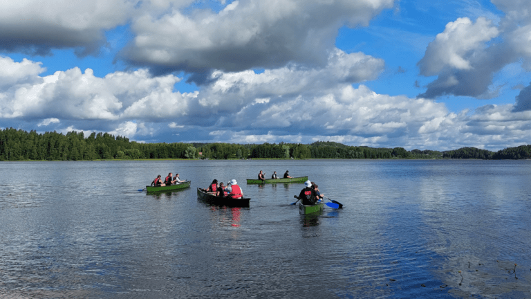 Kuvassa neljä kanoottia kesäisellä järvellä, jokaisessa kanootissa on kolme ihmistä.
