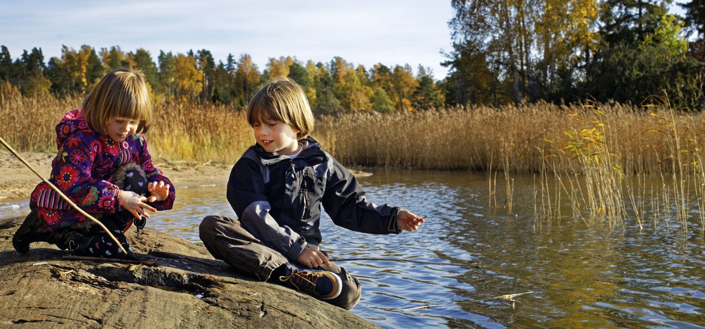 Pieni poika ja pienin tyttö värikäässä takissa leikkivät rantakalliolla