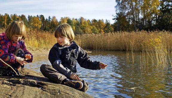 Pieni poika ja pienin tyttö värikäässä takissa leikkivät rantakalliolla