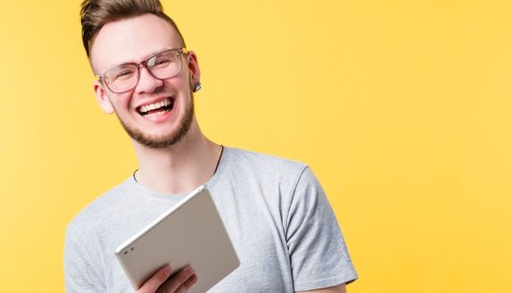 Nuori mies pitää kädessään tablettititokonetta hymyillen.
