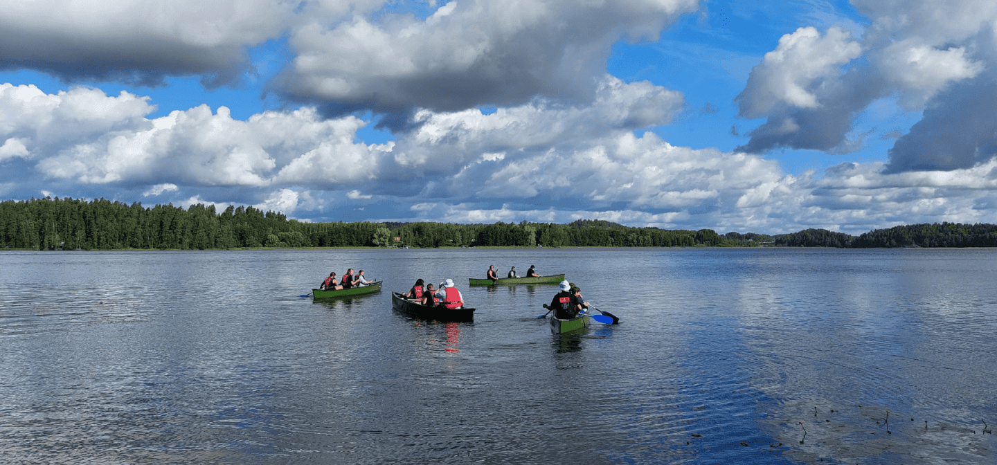 Kuvassa neljä kanoottia kesäisellä järvellä, jokaisessa kanootissa on kolme ihmistä.