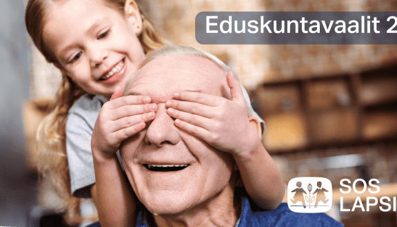 Kuva, jossa leikki-ikäinen tyttö pitää käsiään vanhemman miehen silmien päällä. Molemmat ovat iloisia.