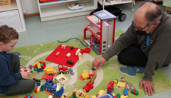 poika ja vanhempi mies leikkivät legoilla matolla