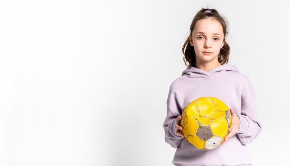 vakavan näköinen tyttö liilassa hupparissa pitää keltaista palloa käsissään