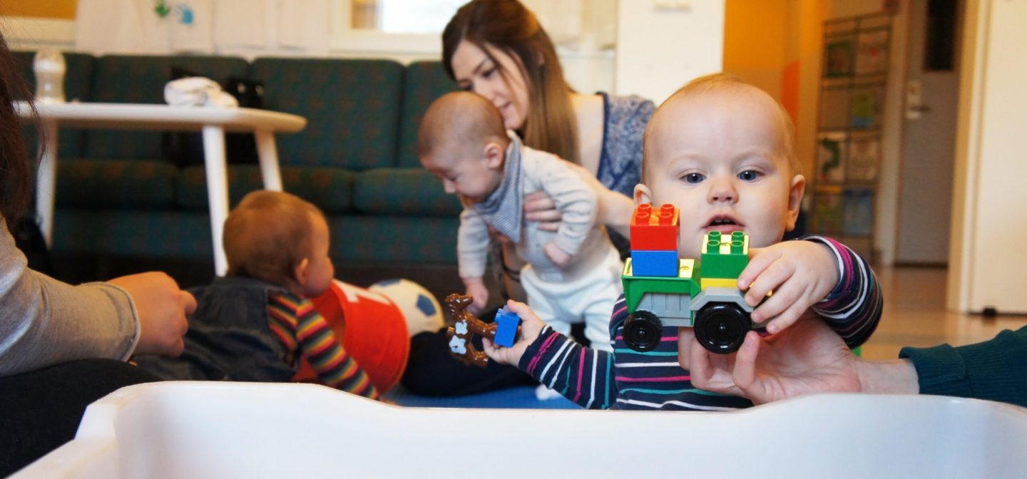 Lapsi leikkii, taka-alalla 'iti toisen lapsen kanssa