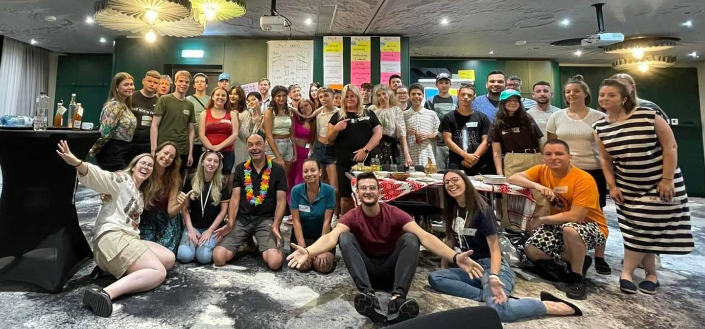 joukko iloisia nuoria poseeraa kameralle, taustalla neuvotteluhuone
