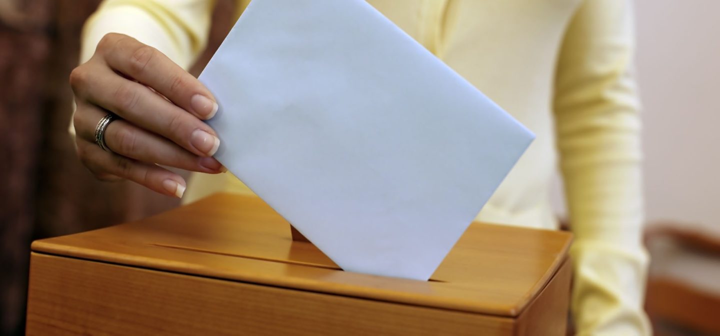 vaaliurna ja naisen käsi, joka laittaa siihen äänestyslipuketta