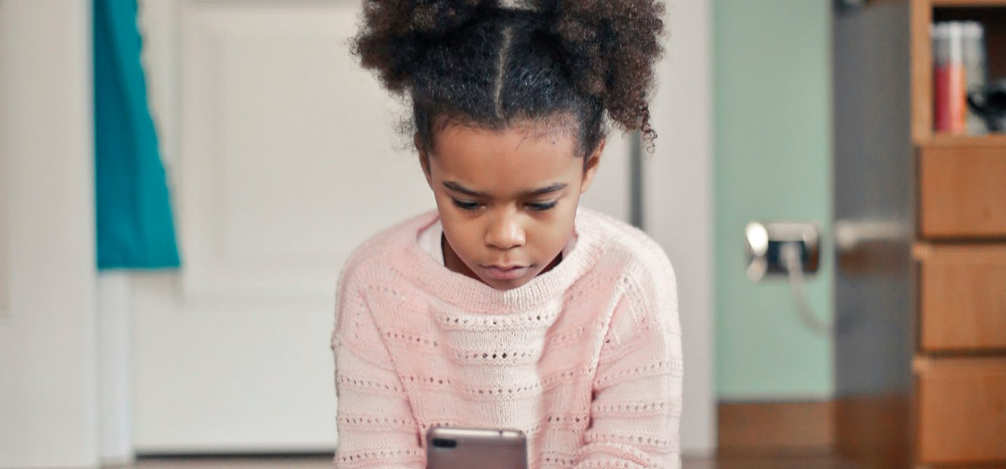 tyttö istumassa huoneen lattialla katsoen puhelinta