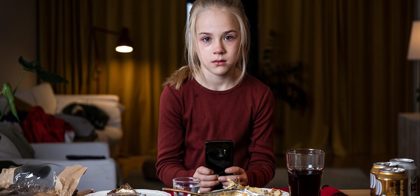 vakava tyttö istuu puhelin kädessä pöydän ääressä ja katsoo kameraan