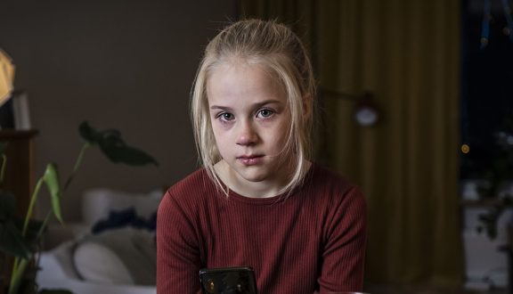 surullisen näköinen tyttö katsoo kameraan kännykkä kädessä
