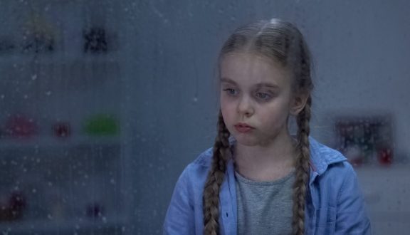 Tyttö surullisen näköisenä pimeässä huoneessa
