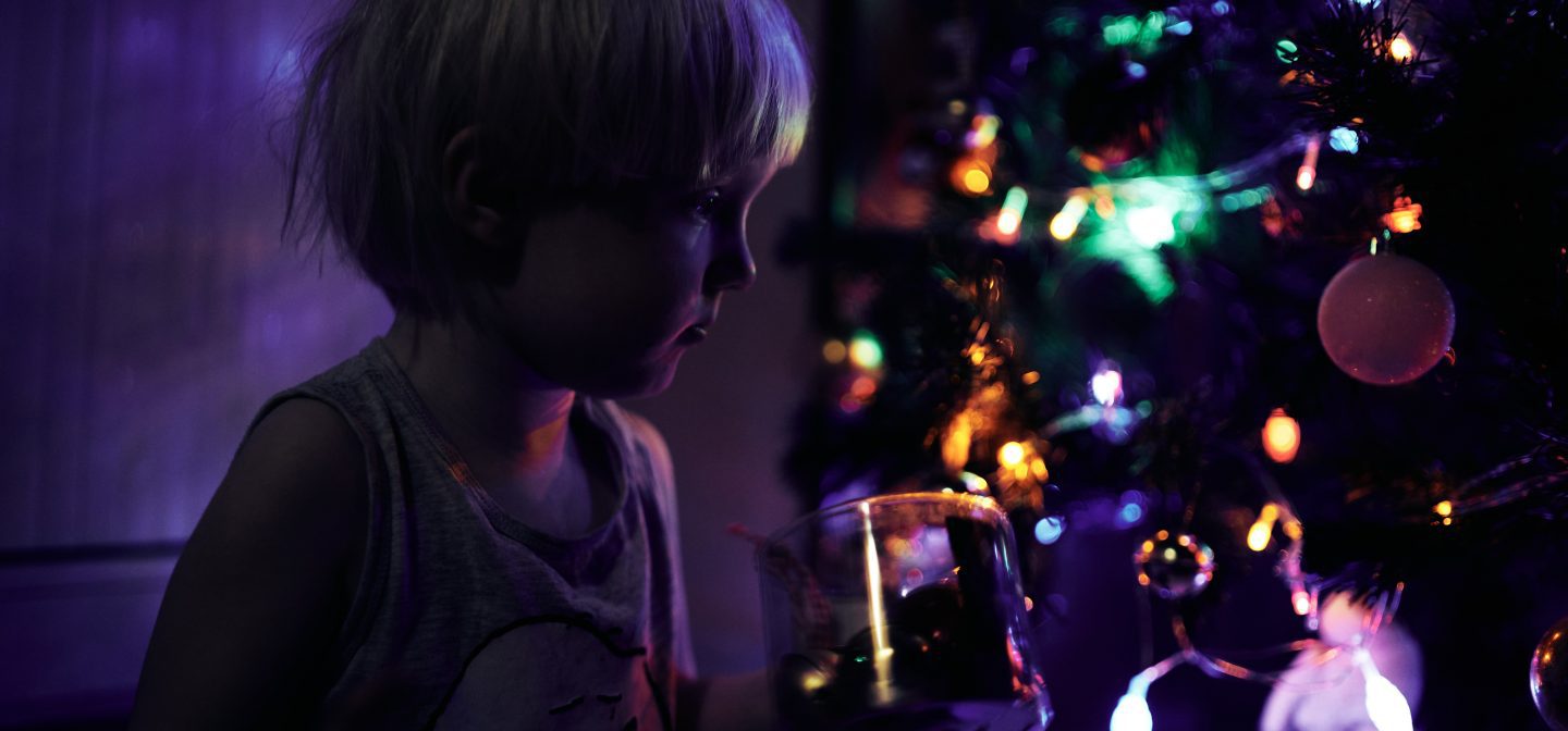 Tyttö joulukuusen edessä pimeässä joulukoristeiden hohteessa.