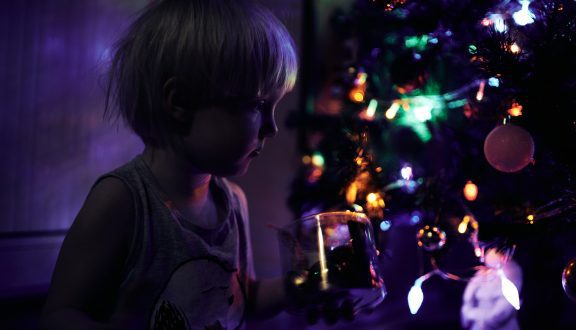 Tyttö joulukuusen edessä pimeässä joulukoristeiden hohteessa.