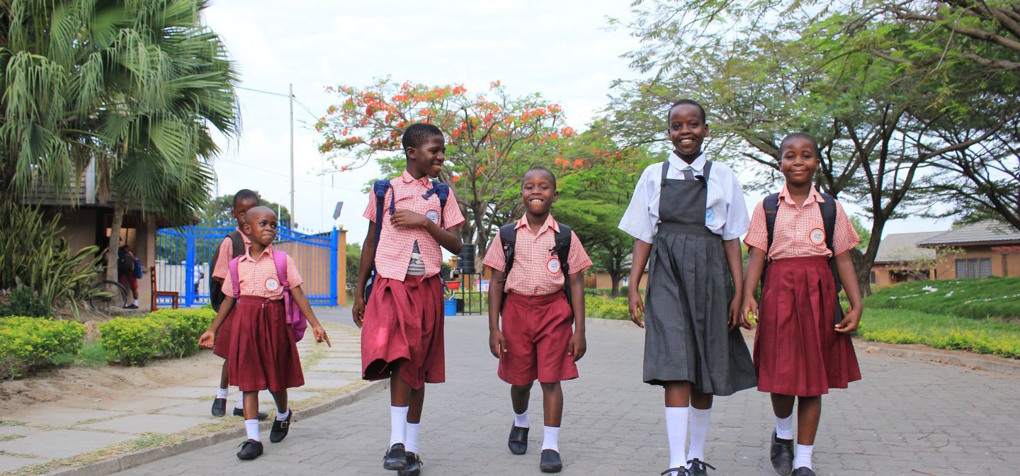 5 lasta kävelemässä kadulla. Yhdellä heistä on valkoinen paita ja harmaa mekko, muilla vaalenpunaista.