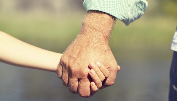 Vanhan miehen käsi pitää lapsen kädestä kiinni