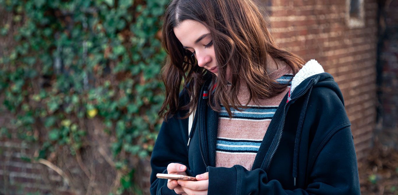 Teini katselee kännykkää ulkona.